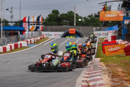 Pilotos disputando corrida em campeonato de kart com vários karts alinhados na pista durante prova de rental kart.