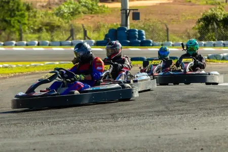 Pilotos de kart disputando posição em curva durante corrida de Rental Kart em pista outdoor, com karts alinhados e competidores usando capacete e equipamentos de segurança.
