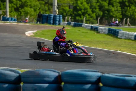 Piloto em curva utilizando luvas de kart, demonstrando controle e precisão na pilotagem em pista outdoor.